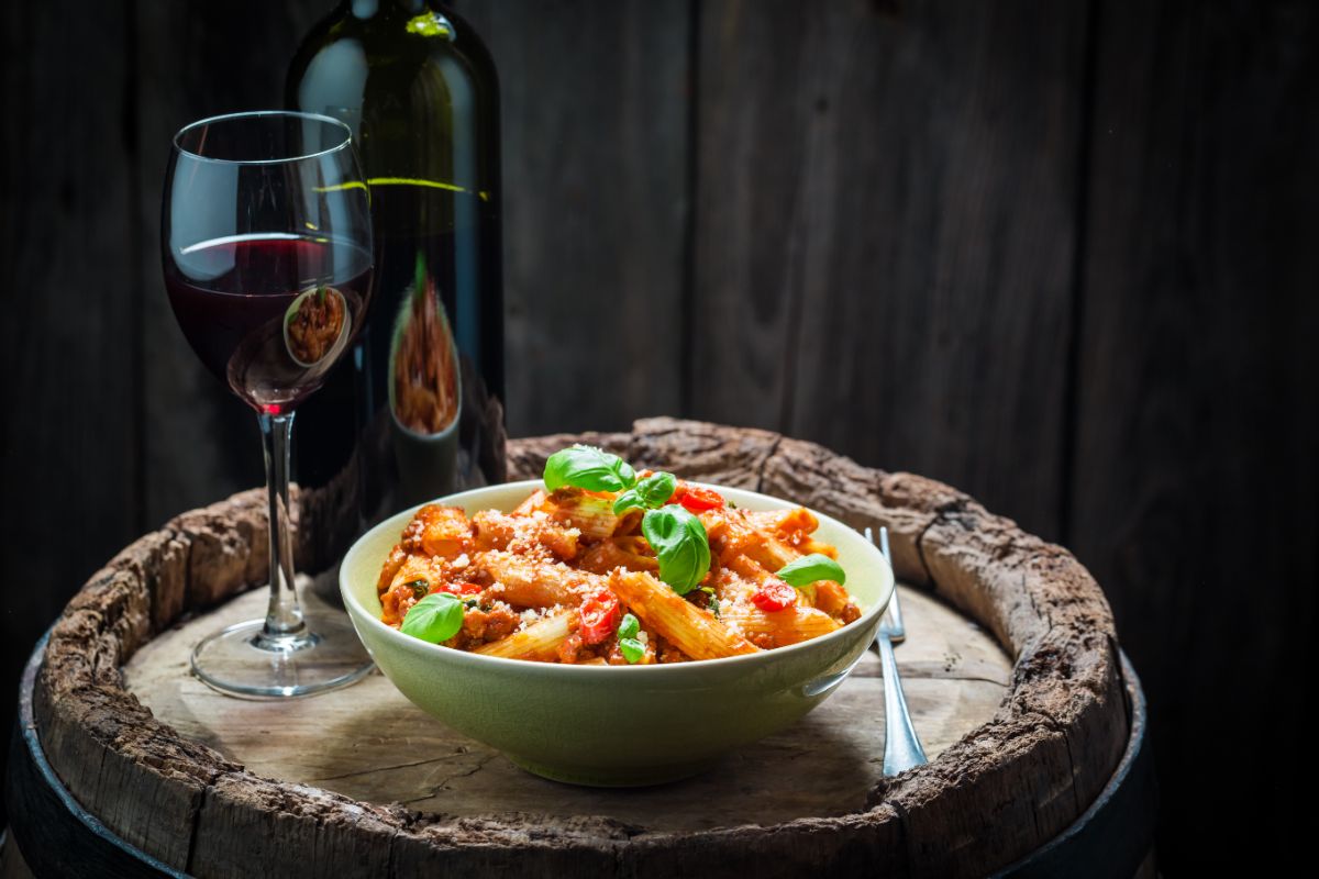 Glas en fles Merlot naast bord pasta op wijnvat
